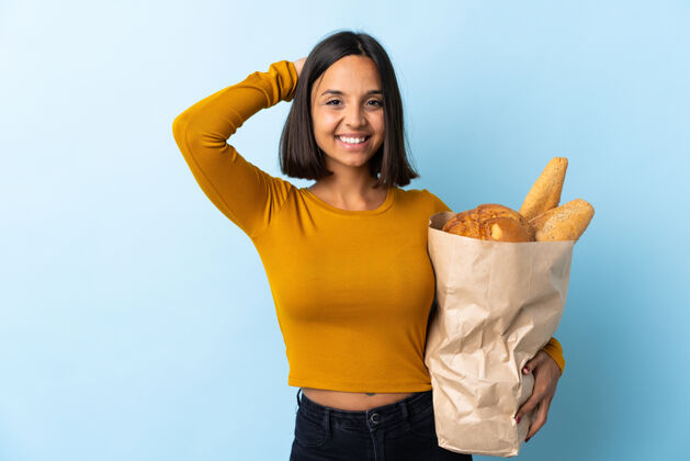 表情一个年轻的拉丁女人在买面包 在蓝色的椅子上笑食物年轻大笑
