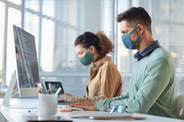 大流行一群戴着面具的程序员坐在桌旁 在流感大流行期间在电脑上处理代码坐着人员通信