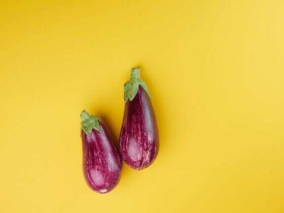 生的一对紫色条纹茄子放在一个黄色的表面上 彼此相邻黄色蔬菜茄子