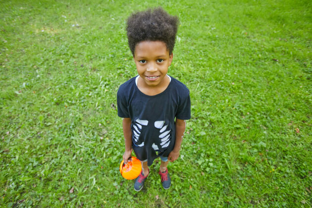 卷发非洲小男孩站在户外绿草上对着镜头微笑的画像童年享受玩耍