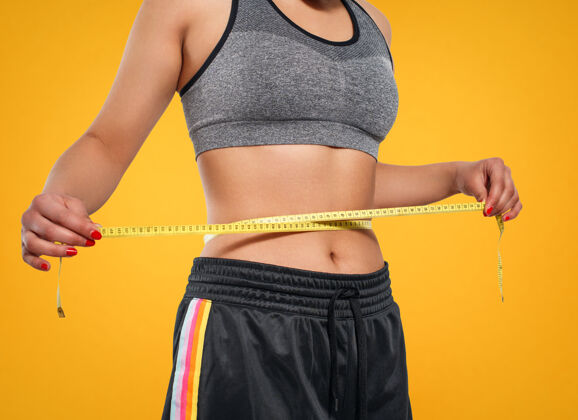 运动苗条女子用卷尺量腰围的特写镜头测量.隔离在黄色背景上身体脂肪团运动