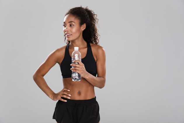 女孩一位微笑的年轻非洲女运动员的肖像 她在灰色的墙上独自训练后休息 手里拿着装满水的瓶子欢呼瓶子人