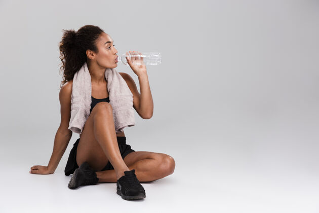 瓶子一位年轻的非洲女运动员在训练后休息的肖像 隔着灰墙 喝水运动员坐着体重