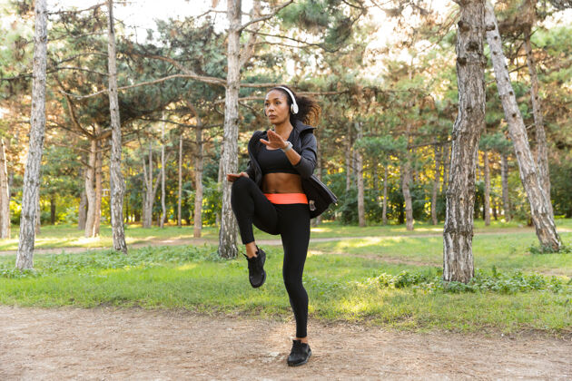 运动一个20多岁的精力充沛的女人穿着黑色运动服 在绿色公园里做运动健身美国年轻