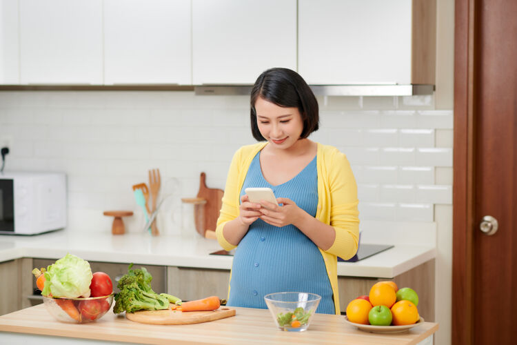 亚洲人孕妇在厨房准备食物 用手机厨房母亲产妇