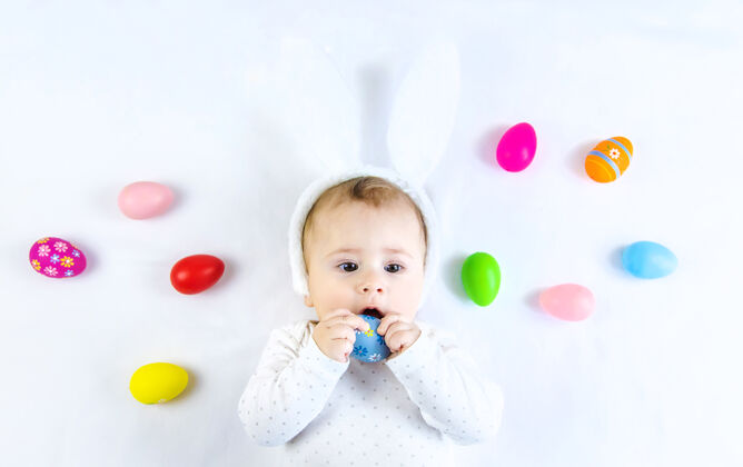 鸡蛋宝宝穿得像兔子 在白色的表面上放复活节彩蛋服装可爱玩