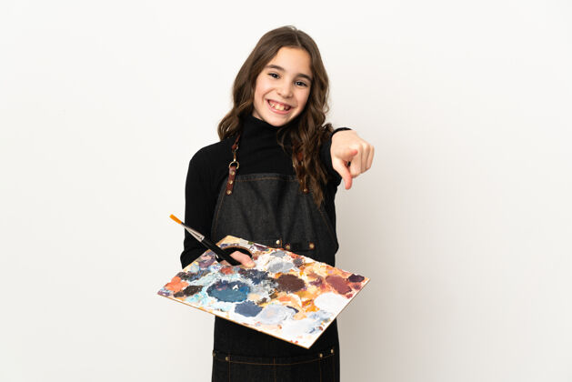 信心小艺术家女人拿着一个调色板孤立地在白色的墙上指着前面的快乐表情可爱年轻画笔