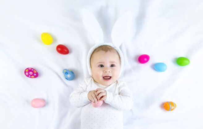 童年宝宝穿得像兔子 在白色的表面上放复活节彩蛋有趣脸人