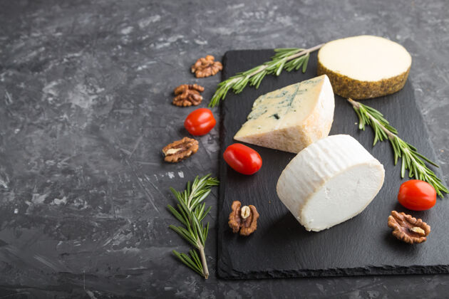 健康白色山羊奶酪和各种奶酪与迷迭香和西红柿在黑色板岩板上的黑色混凝土表面厨房切片板