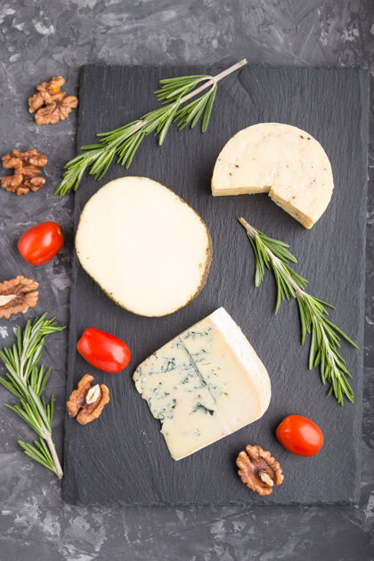 素食蓝色奶酪和各种类型的奶酪与迷迭香和西红柿在黑色板岩板上的黑色混凝土表面顶视图平铺木板