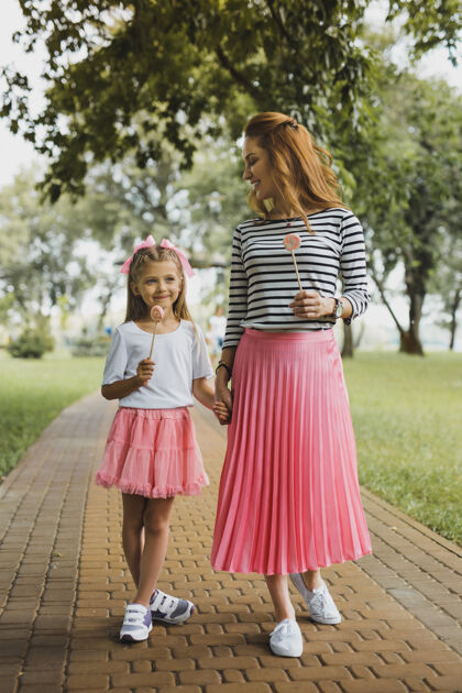 养育家庭装妈妈和女儿穿着粉色裙子和白色运动鞋 同时拥有可爱的家庭装树生态童年