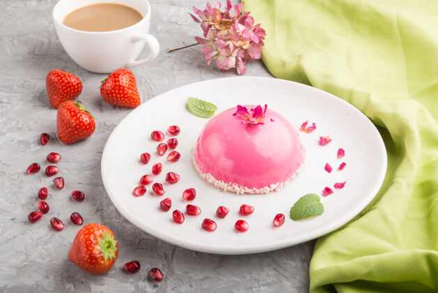 糖粉色的草莓慕斯蛋糕和一杯咖啡放在灰色的水泥表面和绿色的纺织品上蛋白糖健康食物