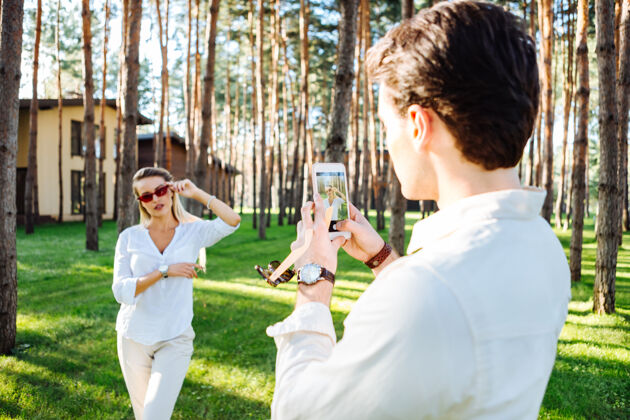 浪漫自然摄影漂亮聪明的男人拿着智能手机给他的女朋友拍照周末传统享受
