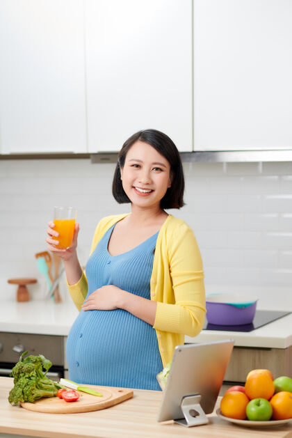 腹部孕妇拿着一杯橙汁在厨房里年轻新鲜饮食