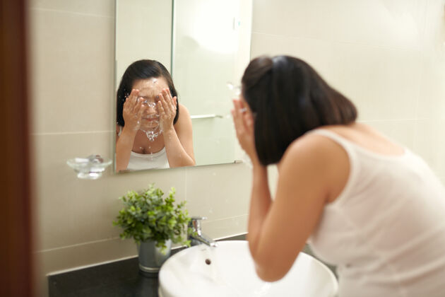 微笑有魅力的女人在涂完面膜后在浴室里洗亚洲健康早晨