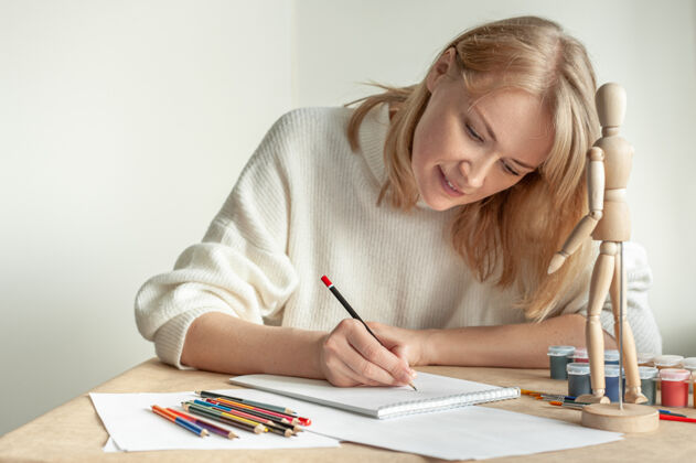 纸一个穿着白色套头衫的金发美女坐在桌边画画人体模型铅笔色彩