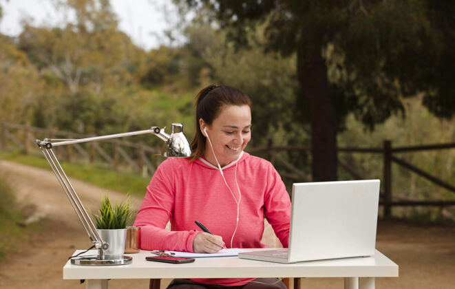 自由职业者自由职业妇女在户外工作 在大自然中的电脑紫红色台灯数码游牧民