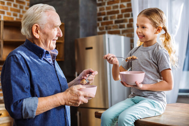 孙子积极可爱的小女孩微笑着和爷爷一起吃早餐家庭人祖父母