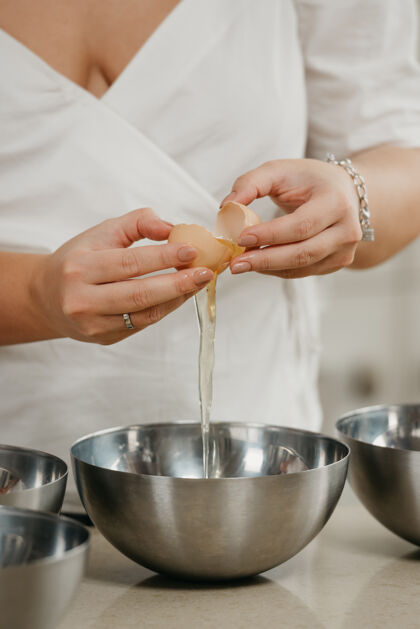 刀厨房不锈钢碗上方 一位年轻女子的手将蛋黄和蛋清分开的近照鸡蛋准备烹饪