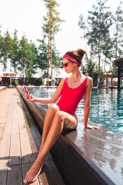 比基尼时尚博主坐在游泳池旁为社交网络拍照的迷人磁性女人热漂亮酒店
