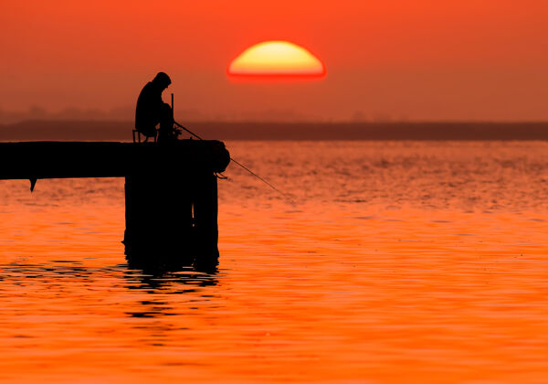 鱼在旭日和柔和的红光中 渔夫的身影人放松渔民