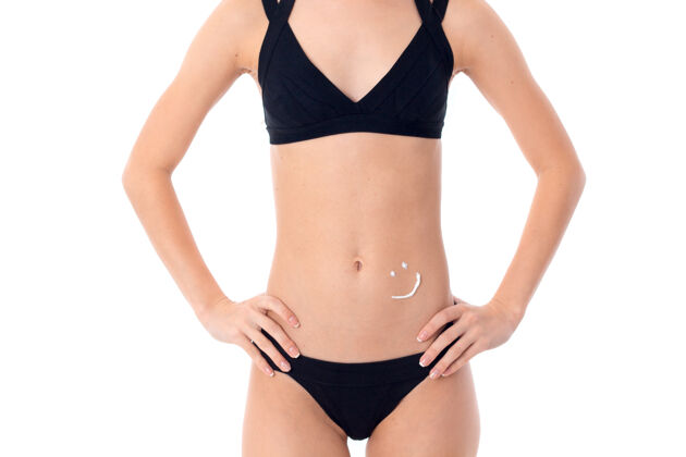 快乐穿着黑色泳衣的年轻女子 腹部涂着护肤霜 隔离在白墙上模特漂亮太阳镜