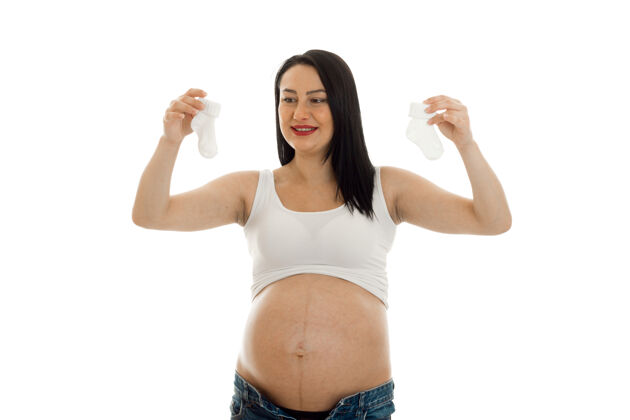女性年轻的黑发孕妇 双手拿着小白袜子 孤零零地站在墙上女人可爱肚子