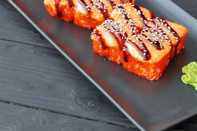 食物烤寿司卷放在木桌上的黑盘子里Maki鱼日式