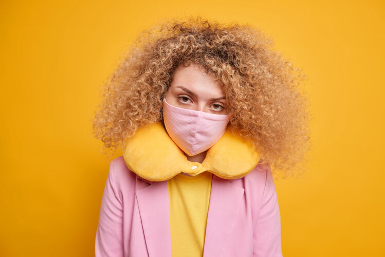 预防病毒爆发期间的安全措施严肃的女人看起来自信地戴上防护面具 以配合衣服颈部枕头姿势对生动的黄色墙壁锁定和covid19脸流感穿着