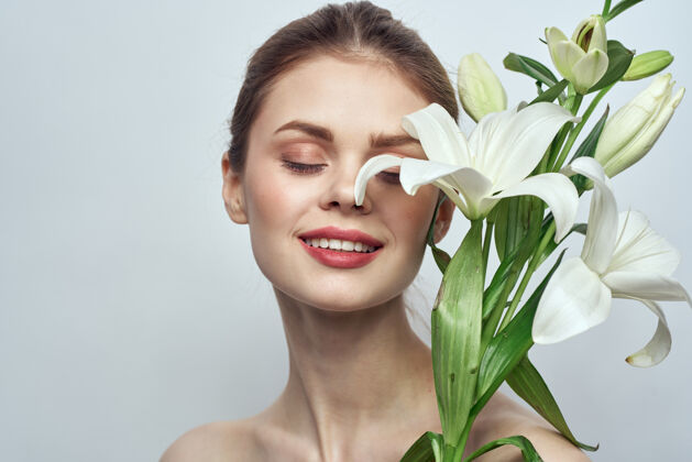 模特美丽的女孩用一束白色的花在浅色的背景上赤裸的双肩清洁皮肤姿势女士肖像