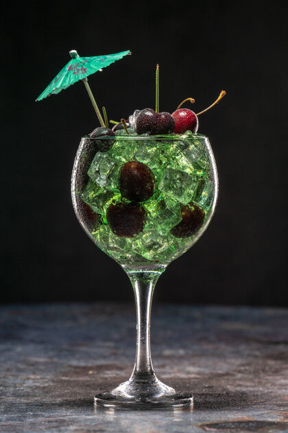 液体绿色鸡尾酒加冰块和樱桃放在一个用伞装饰的玻璃杯里新鲜俱乐部特写