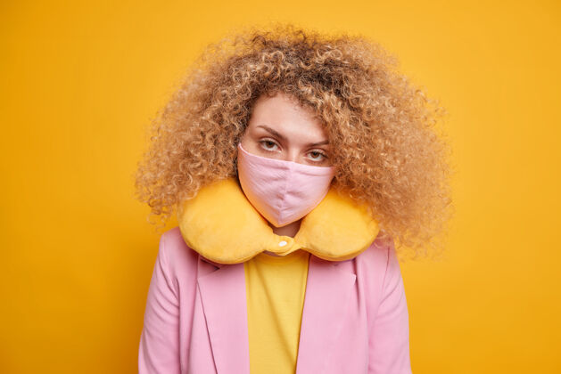 预防病毒爆发期间的安全措施严肃的女人看起来自信地戴上防护面具 以配合衣服颈部枕头姿势对生动的黄色墙壁锁定和covid19脸流感穿着