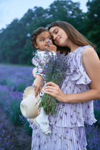 自然快乐的年轻母亲手持薰衣草花束和孩子女孩新鲜花