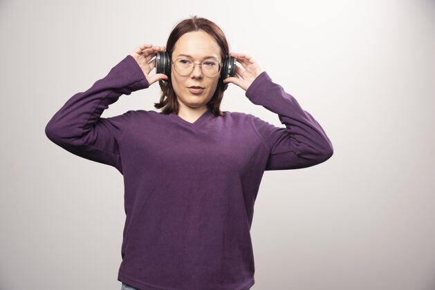 站立戴着眼镜的年轻女子戴着耳机在听音乐 这是一张高质量的白色照片时尚女人肖像