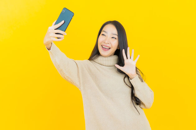 消息画像美丽的亚洲年轻女子微笑着在黄色的墙上智能手机漂亮微笑应用程序