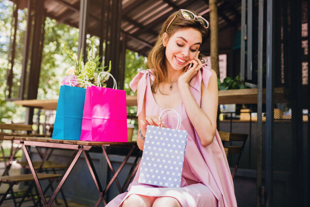 购物一幅年轻的笑容可掬的迷人女子坐在咖啡馆里拿着购物袋打电话的画像太阳镜衣服时尚