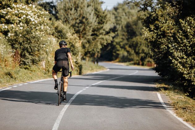 短跑在阳光明媚的日子里 穿着运动服和头盔骑自行车的男运动员的后视图自行车人活动