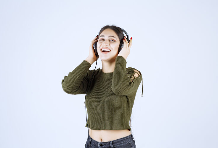 人戴着耳机听音乐的年轻女孩的肖像 并给出了“确定”的标志音乐时尚女士