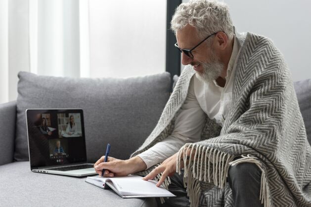 家庭在家学习笔记本电脑和做笔记的老人成熟眼镜男人