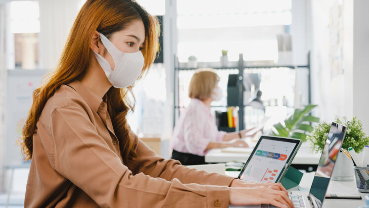 工作亚洲女企业家戴着医用面罩在新的正常情况下保持社会距离以防病毒 同时在办公室使用笔记本电脑行政人员休闲员工