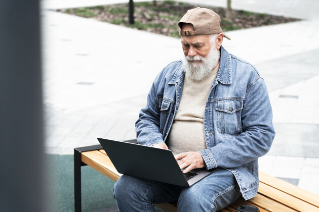 水平在城市户外使用笔记本电脑的老人老年人笔记本电脑户外
