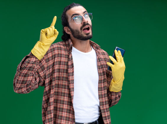 手套年轻帅气的清洁工穿着t恤 戴着手套 拿着电话点站在绿色的墙上印象年轻点