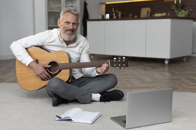 内部大四的男人在家地板上学吉他家庭老年人学习