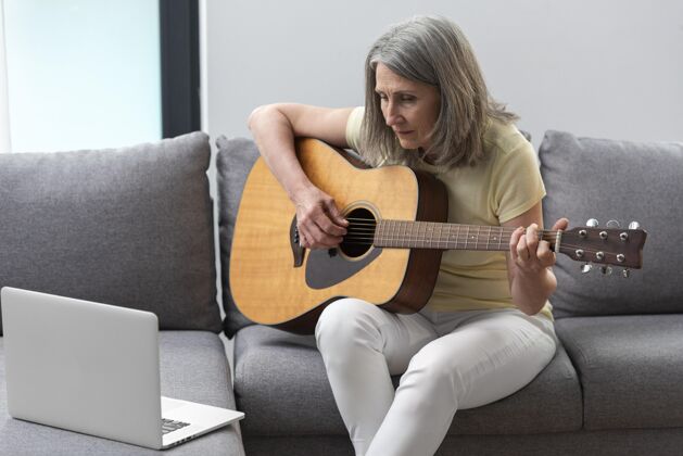 家庭资深女士在家沙发上用笔记本电脑上吉他课里面室内老年人