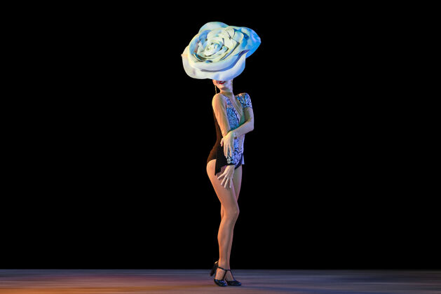 移动年轻的女舞者戴着巨大的花帽在霓虹灯下在黑墙上跳舞花表演女人
