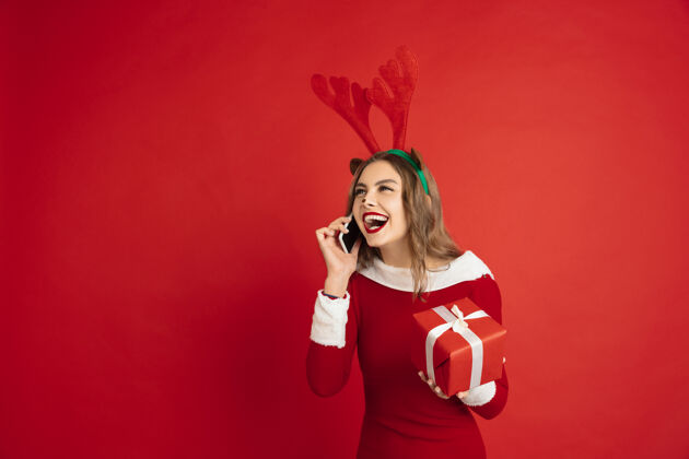 积极带礼物讲电话圣诞节 新年 冬天 假期的概念美丽的白种女人 长发像圣诞老人的驯鹿抓礼物盒年肖像圣诞节