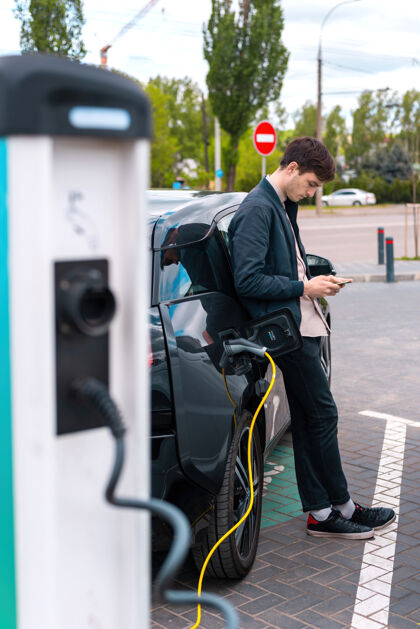 未来男人在充电站给他的电动车充电 用智能手机科技科技设备