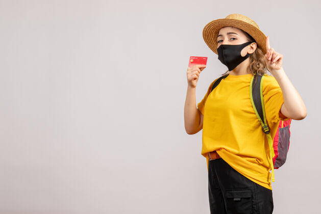 黑人正面图：戴着黑色面具和背包的年轻女子手持卡片面罩旅游流行病