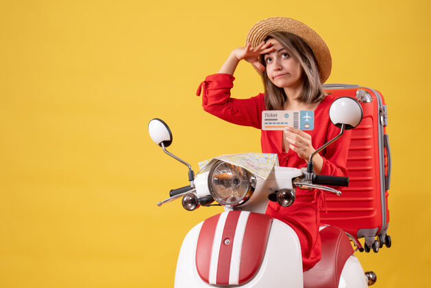 度假正面图：穿着红衣服的年轻女士 手持车票 坐在轻便摩托车上观察旅游旅游旅行者
