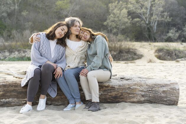妈妈妈妈和她的两个女儿一起在沙滩上度过时光团结拥抱海滩